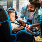 smiling father fastening son in safety seat in car