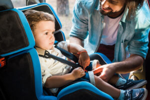 smiling father fastening son in safety seat in car