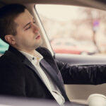 Sleepy man driving car and drinking first morning coffee