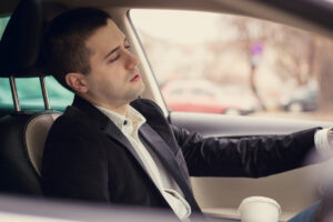 Sleepy man driving car and drinking first morning coffee